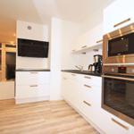 Kitchen with white cabinets, stainless steel oven and microwave. Wooden floor, view into living area.
