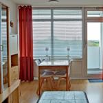 Dining area with table, chairs, and view to balcony. Red curtains and wooden floor.