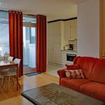 Living area with red sofa, dining table, and kitchenette.