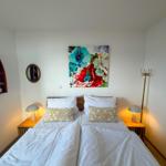 Room with double bed, nightstands, wall art, and decorative items.