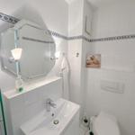 Bathroom with sink, mirror, and toilet. White tiles and blue decorative strip.
