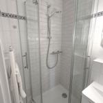 Shower cabin with glass door, showerhead, and handheld shower, white tiles, and towel rack.