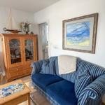 Living room with sofa, wooden cabinet, and wall painting. Wooden floor and rug.