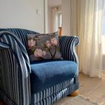 A blue striped armchair with a floral cushion stands near a window with curtains.
