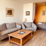 Living area with sofa, armchair, and wooden table. Bedroom with bed visible in background.