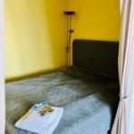 Bedroom with yellow walls, bed with gray quilted cover, and floor lamp.