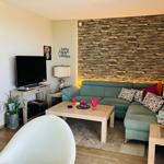 Ein Wohnzimmer mit grünem Sofa, Holztisch und Steinwand im Hintergrund.