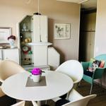Runde weiße Tisch mit Stühlen, Vitrine, Bilder und grüner Sessel mit Kissen.