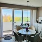 Essbereich mit runder Tisch und vier Stühlen, großes Fenster mit Blick auf Grünfläche.