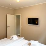 Bedroom with bed, towel stack, and wall-mounted TV. Door leads to adjacent room.