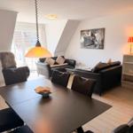 Living and dining area with sofa, dining table, and kitchenette. Window to outdoor terrace.