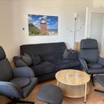Living room with sofa, two chairs, and round table. Wall picture shows lighthouse.