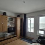 Living room with wooden furniture, TV, and sea view through windows and balcony door.