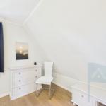 Schlafzimmer mit weißem Schrank, Stuhl und Wandbild. Fenster mit blauen Vorhängen.
