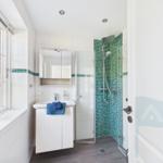 Badezimmer mit Dusche, Waschbecken und Fenster. Duschwand mit grünem Mosaik.