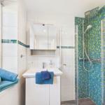 Badezimmer mit Dusche, Waschbecken und Fenster. Mosaikfliesen an der Duschwand.