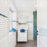 Badezimmer mit Dusche, Waschbecken und Heizkörper. Blaue Handtücher und Mosaikfliesen.