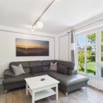 Wohnzimmer mit grauem Sofa, weißem Tisch und Fenster zur Terrasse.