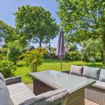Garten mit Sitzgruppe, Tisch und Schirm. Grünfläche und Bäume im Hintergrund.