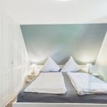 Schlafzimmer mit Doppelbett, Nachttischen und Lampen. Wand in Blautönen. Kleiderkammer und Vorhang.
