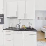 Kitchen with white cabinets, sink, and cooktop. View into bedroom with bed.