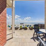 Terrace with table and chairs, view of beach and sea under blue sky.