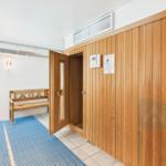 Sauna room with wooden wall and bench. Door open, floor with blue mat.
