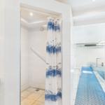 Shower with curtain, blue mat, and bathtub in the background.