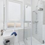 Bathroom with shower, sink, and window with blinds.