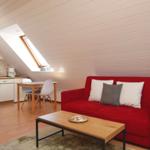 Ein Wohnbereich mit rotem Sofa, Holztisch und Dachschrägen. Küchenbereich mit Tisch und Stühlen.