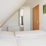Schlafzimmer mit Dachschräge, Bett, Schrank und Wandbild.