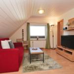 Ein Wohnzimmer mit rotem Sofa, TV und Holzmöbeln unter einer schrägen Decke.