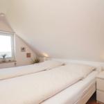 Schlafzimmer mit Doppelbett, Nachttisch und Fenster unter Dachschräge.