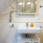 Waschbecken mit Spiegel, Handseife und Blumenvase an der Wand.