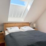 Schlafzimmer mit Dachschrägen, Bett, Nachttisch und Dachfenster mit Jalousie.