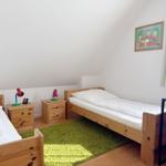 Zwei Einzelbetten, Nachttische mit Lampen, grüner Teppich, Wandbild und Fenster mit Vorhängen.