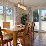 Esszimmer mit Holztisch, Stühlen und Blick auf Balkon.