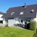 Modernes Haus mit Garten, Terrasse und Grill. Dach mit Dachfenstern und Satellitenschüsseln.