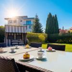 Terrasse mit Esstisch, Sonnenliege und Kuchen unter blauem Himmel.