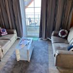 Two sofas with cushions surround a white coffee table. A balcony is accessible through the glass door.