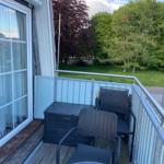 Terrace with two chairs, table, and storage box. View of green trees and lawn.