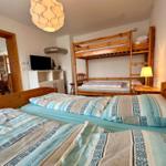 Zimmer mit zwei Einzelbetten und einem Holz-Kinderstockbett. Fernseher und Tischlampe sind vorhanden.