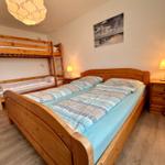 Zimmer mit Doppelbett, Etagenbett und Nachttisch mit Lampe.