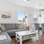 Wohn- und Essbereich mit grauem Sofa, weißem Tisch und Küchenbereich.