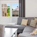 Grauer Sofa-Set mit Kissen und Tisch. Durch Fenster Blick auf Garten und Haus.