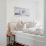 Schlafzimmer mit weißem Bett, dekorativer Wandkunst und Nachttisch mit Lampe.