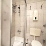 Dusche mit Duschbrause, Toilette und Heizkörper an der Wand.