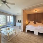 Ein Schlafzimmer mit Doppelbett und Wohnbereich mit Glas-Tisch und Balkon.