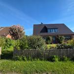 Haus mit Gartenzaun, Blumen und Baum unter blauem Himmel.