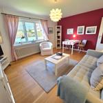 Wohn- und Essbereich mit Sofa, Tisch und Fenster. Rote Wand und Holzboden.